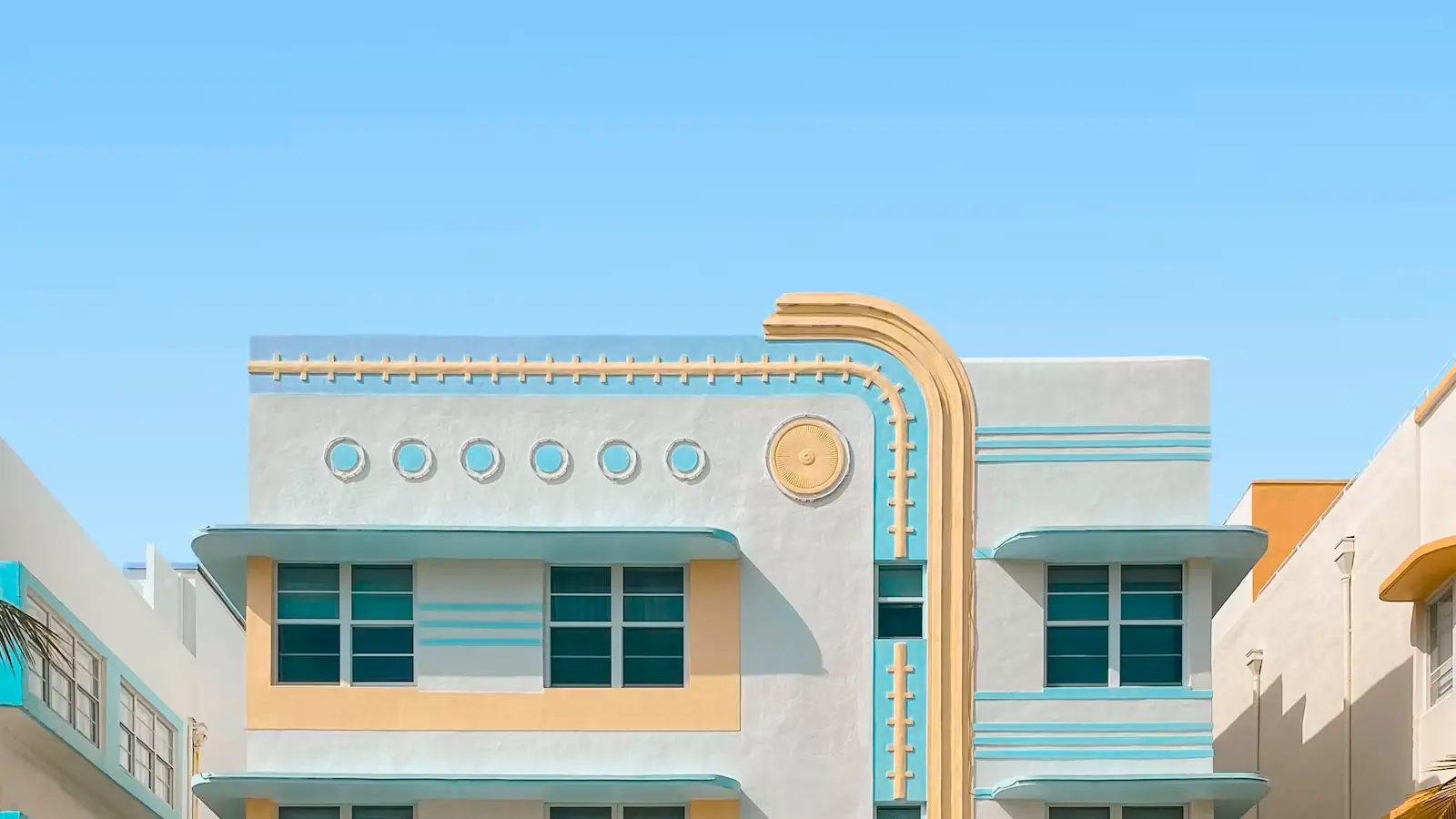 The symmetrical pastel facade of a 1930s Art Deco hotel on Ocean Drive under a clear sky