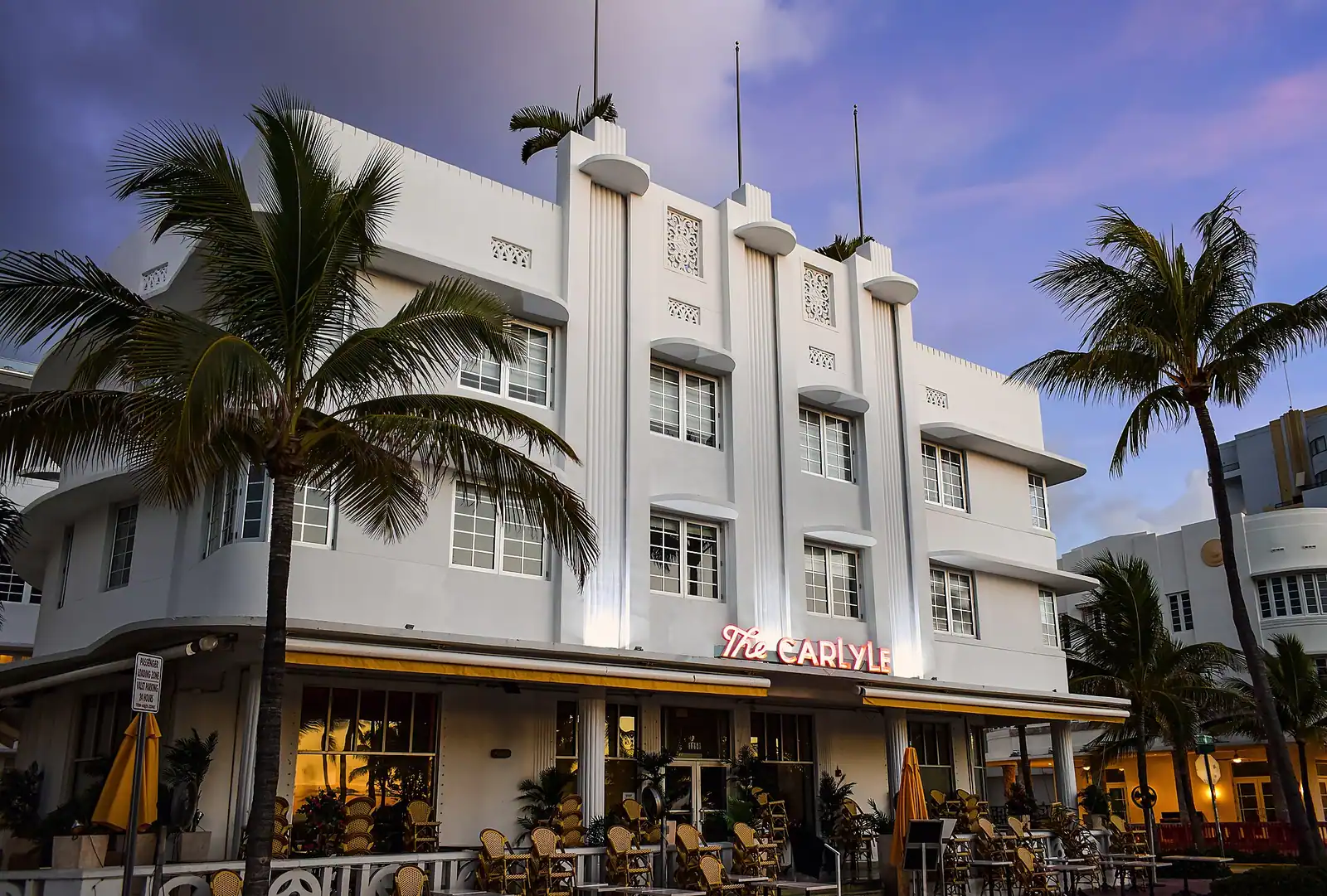 A symmetrical pastel hotel facade with banded concrete window shades and a stepped central parapet
