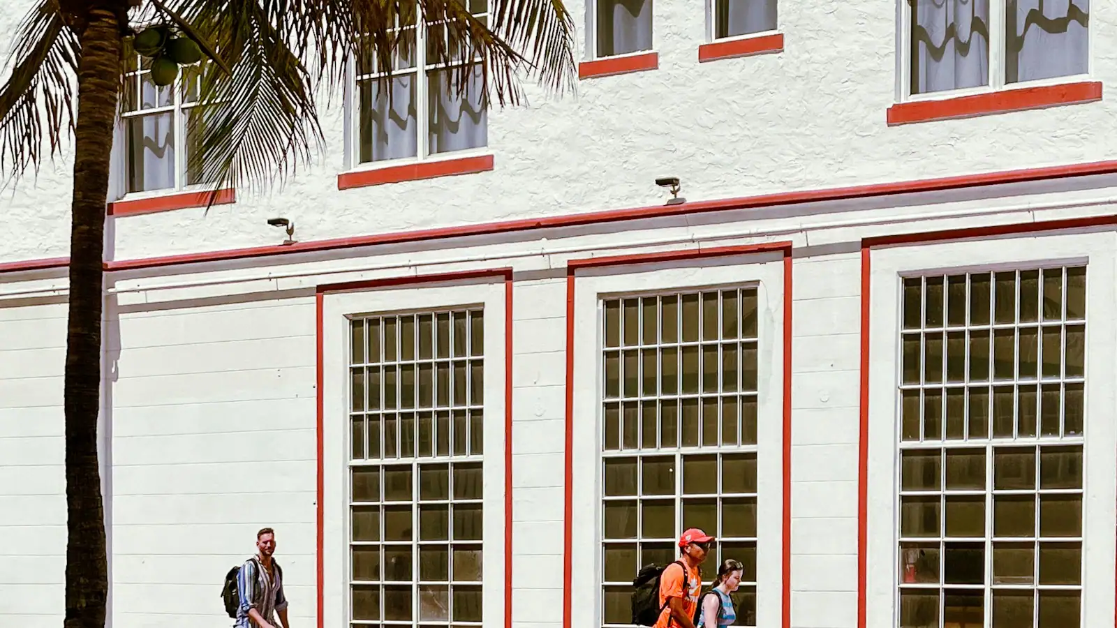 People walking past a tall white building on a Miami Beach street