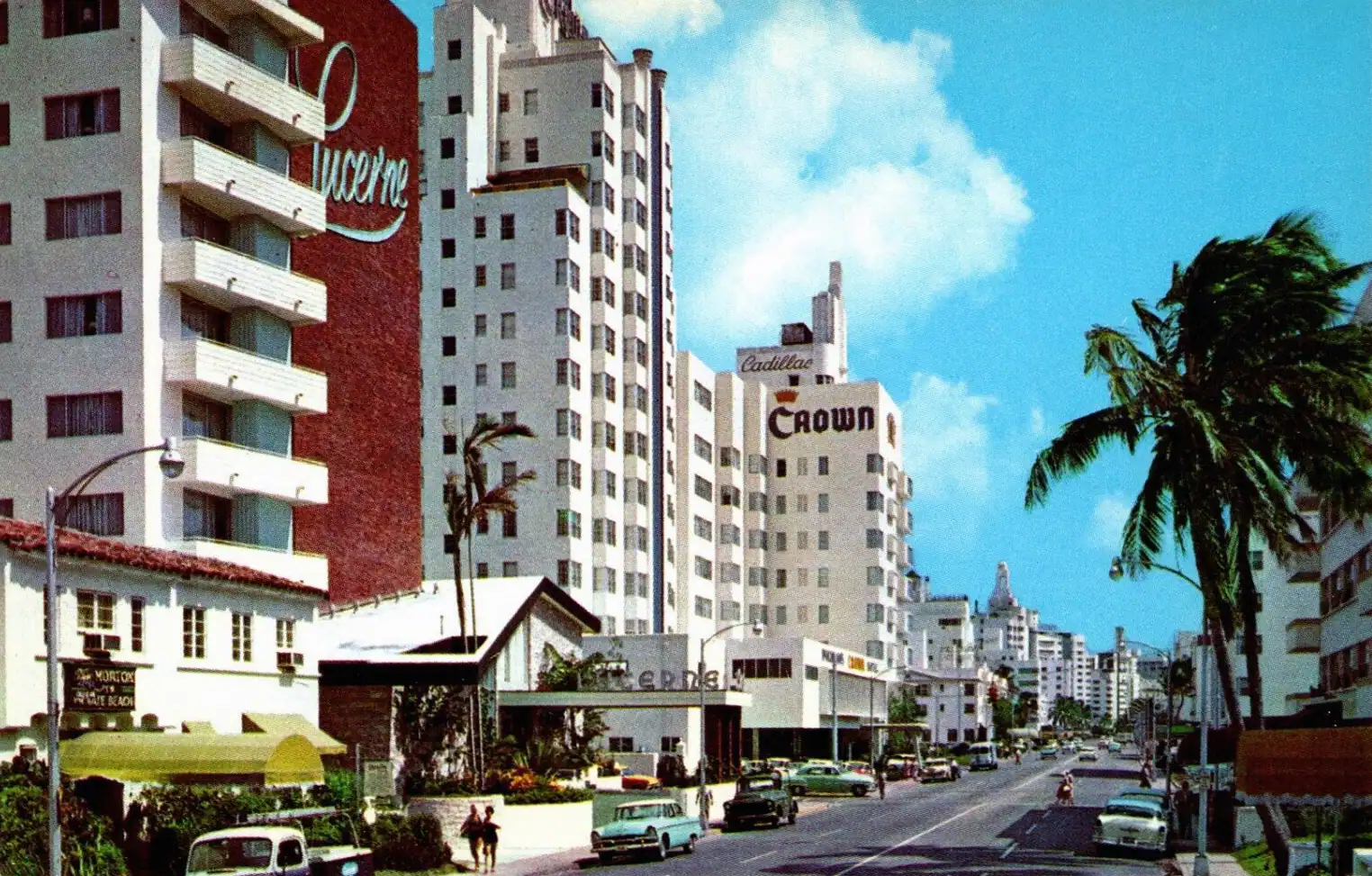 A palm-lined beach in front of a row of mid-rise hotel buildings