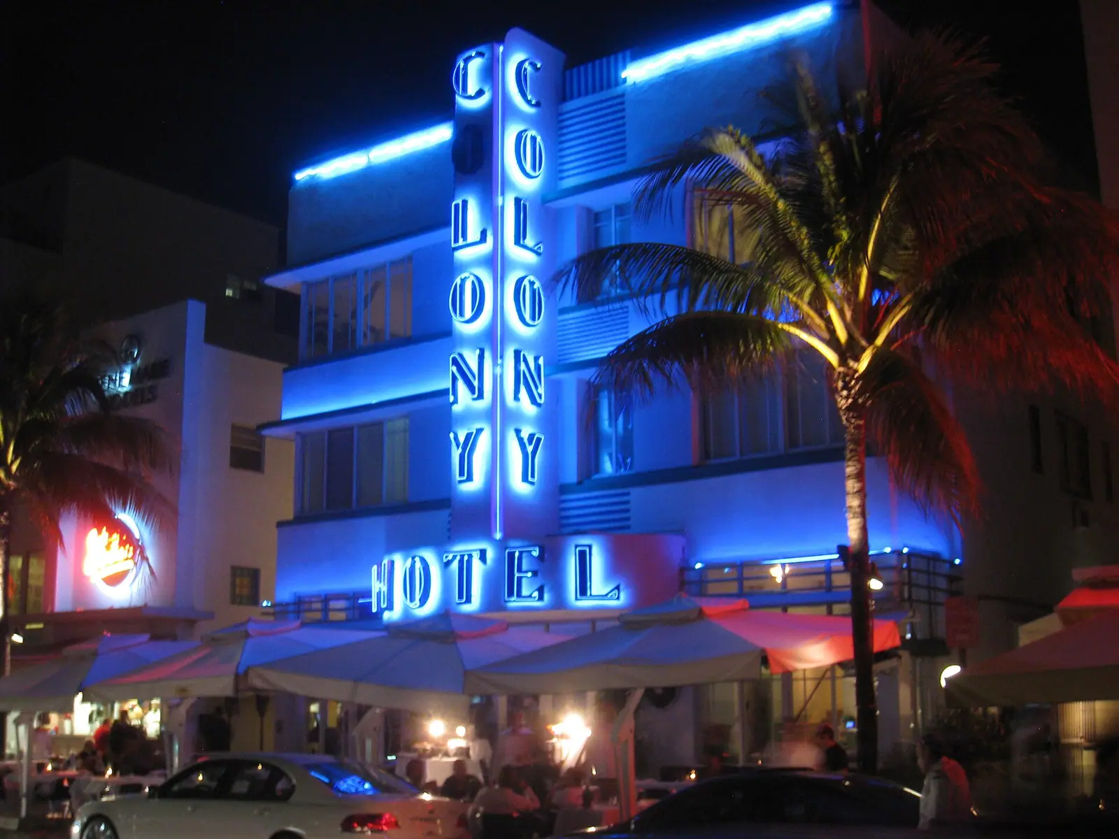 The peach and mint facade of a three-storey Art Deco hotel seen from below with a palm frond crossing the frame
