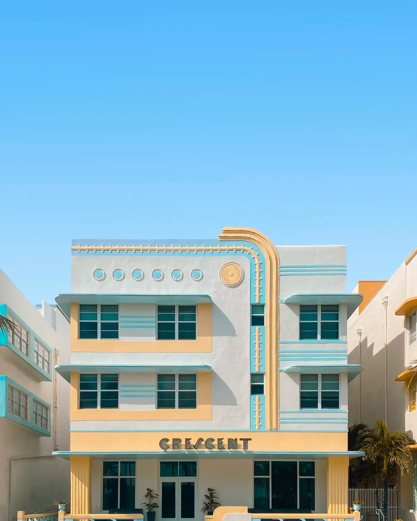 The symmetrical pastel facade of a 1930s Art Deco hotel on Ocean Drive under a clear sky