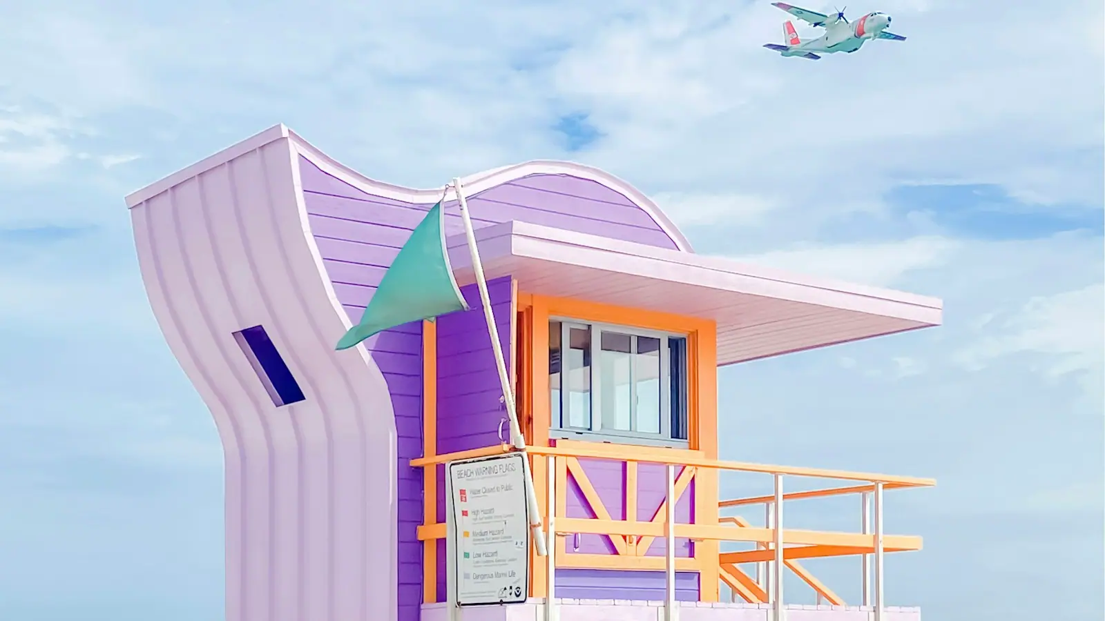 A lifeguard stand on the sand at Miami Beach with a plane passing in the sky behind it