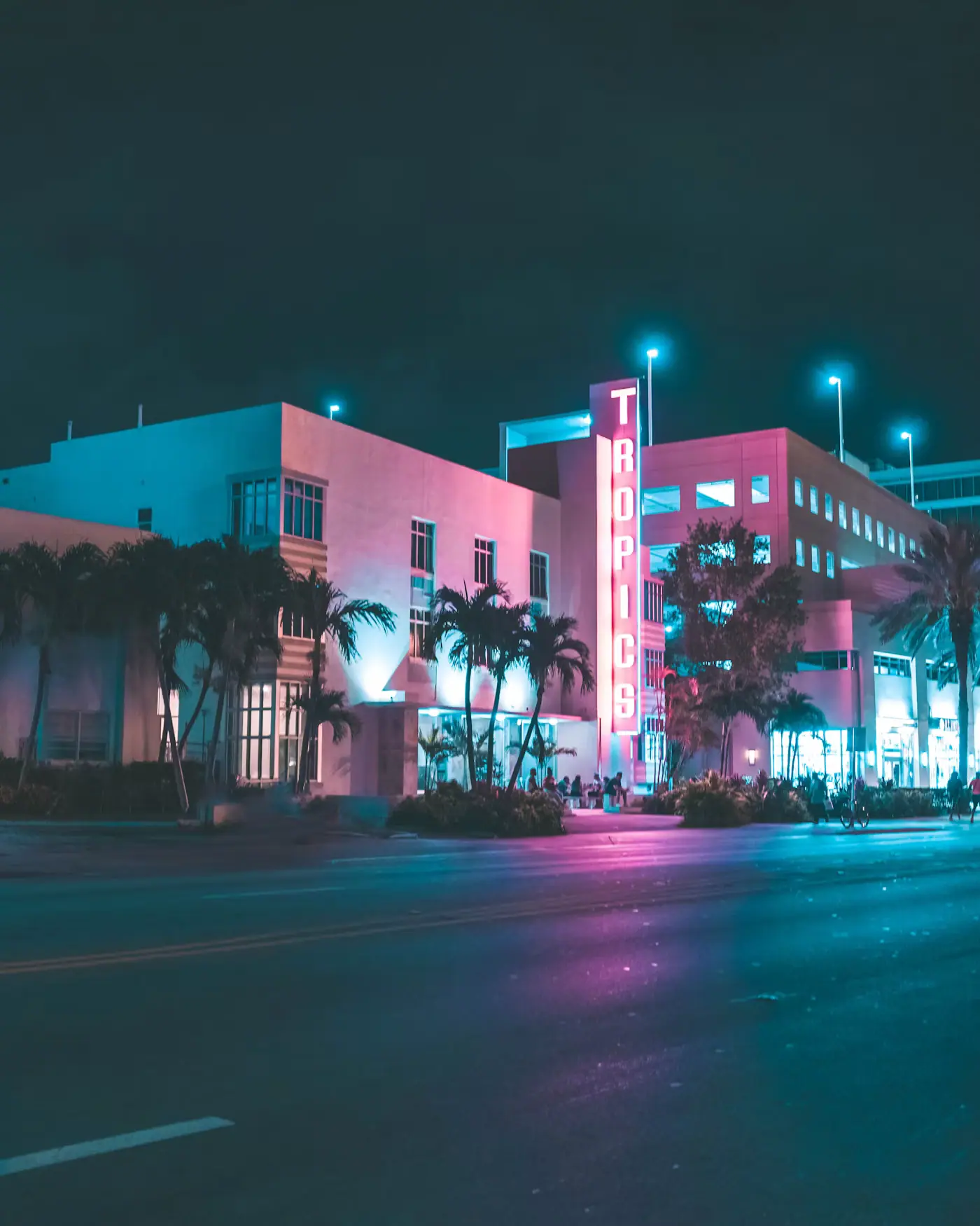 A neon-lit Art Deco hotel on a palm-lined Miami Beach street at night
