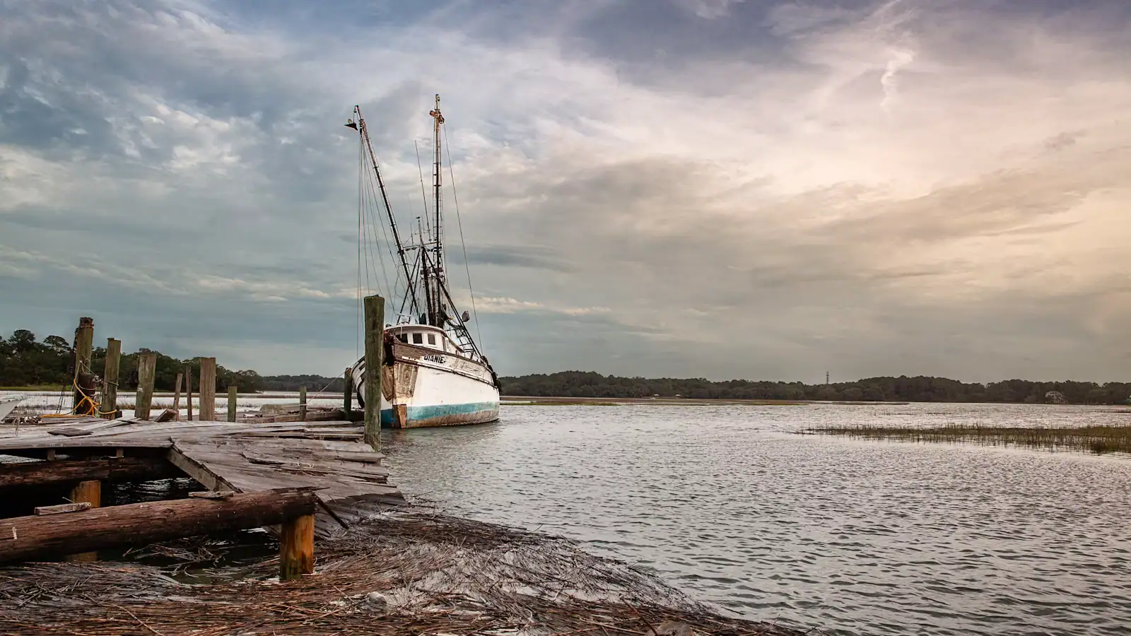 A working boat tied up at a weathered timber dock under a heavy sky