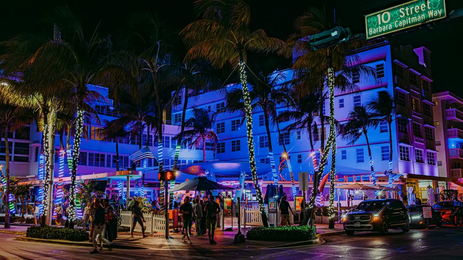 A city street after dark with neon-lit building frontages and palm trees
