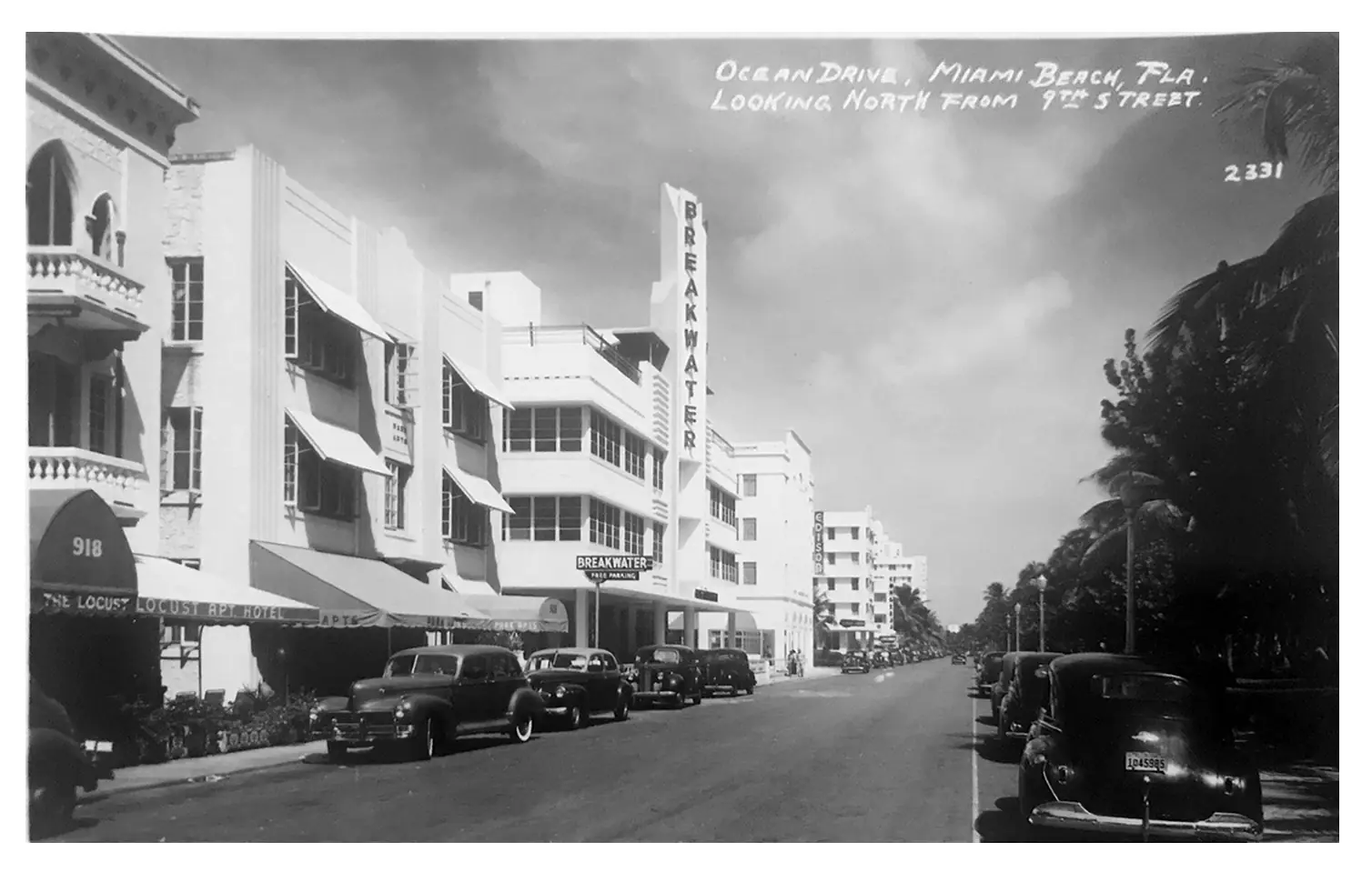 The peach and mint facade of a three-storey Art Deco hotel seen from below with a palm frond crossing the frame