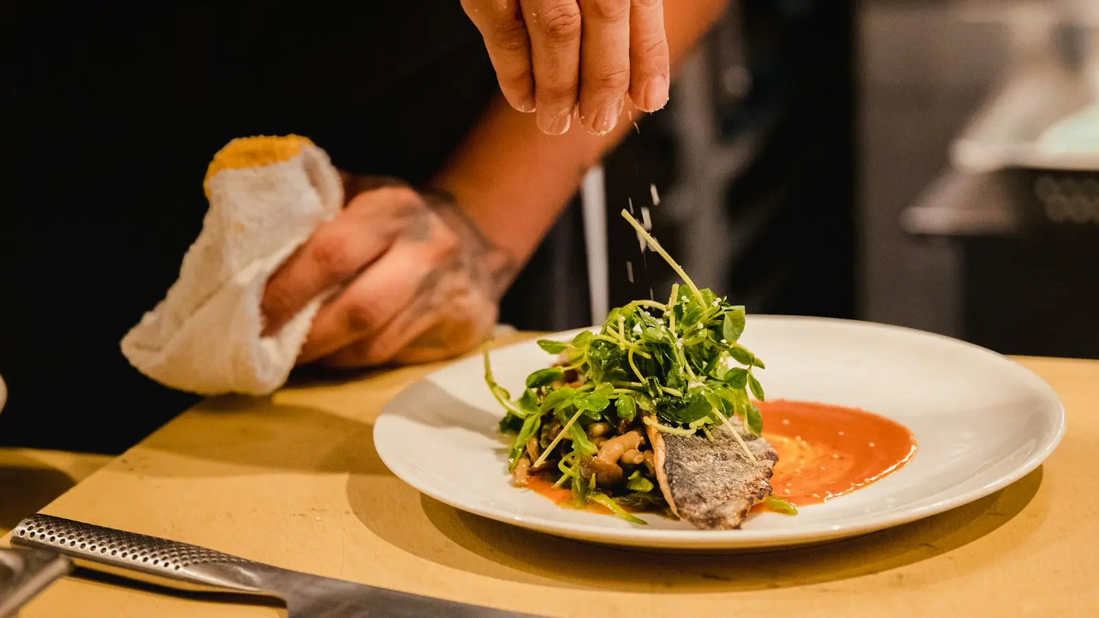 A cook finishing a plated seafood dish in a restaurant kitchen