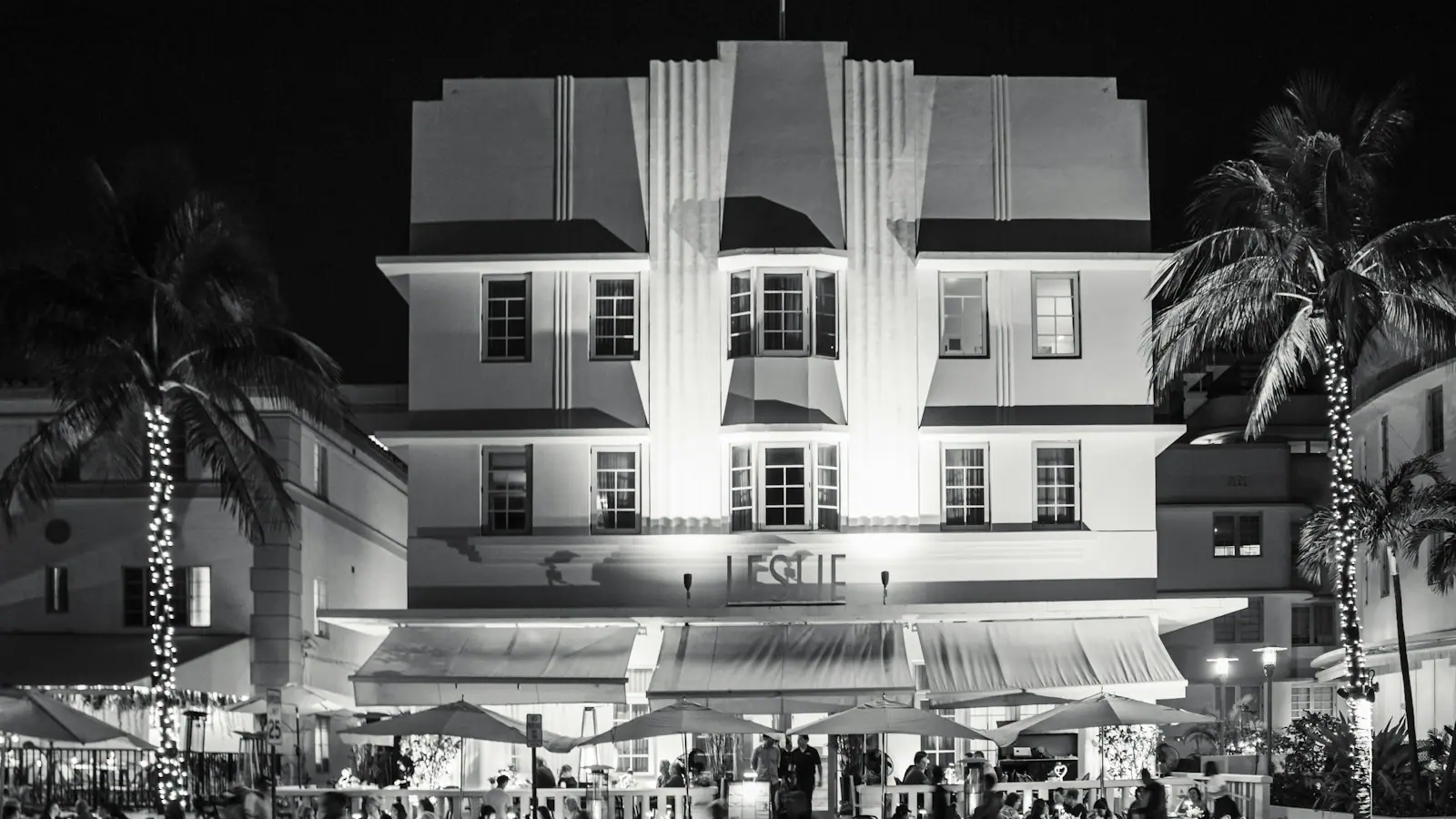 A brightly lit building facing a crowded Miami Beach street at night
