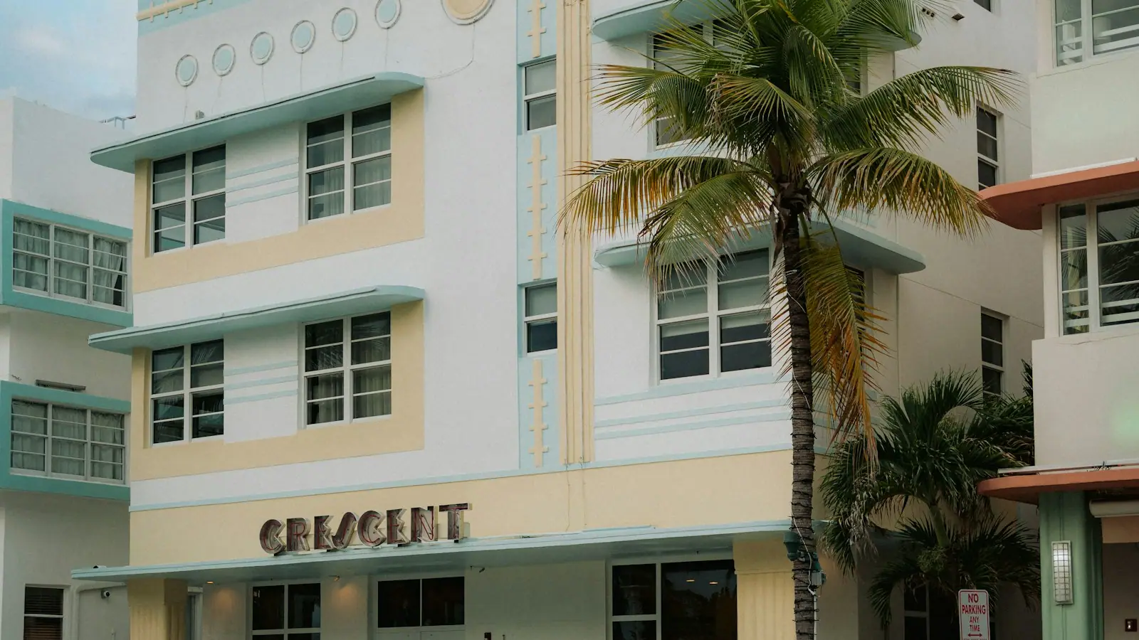 A pastel Art Deco hotel façade with a palm tree in front of it on a Miami Beach street