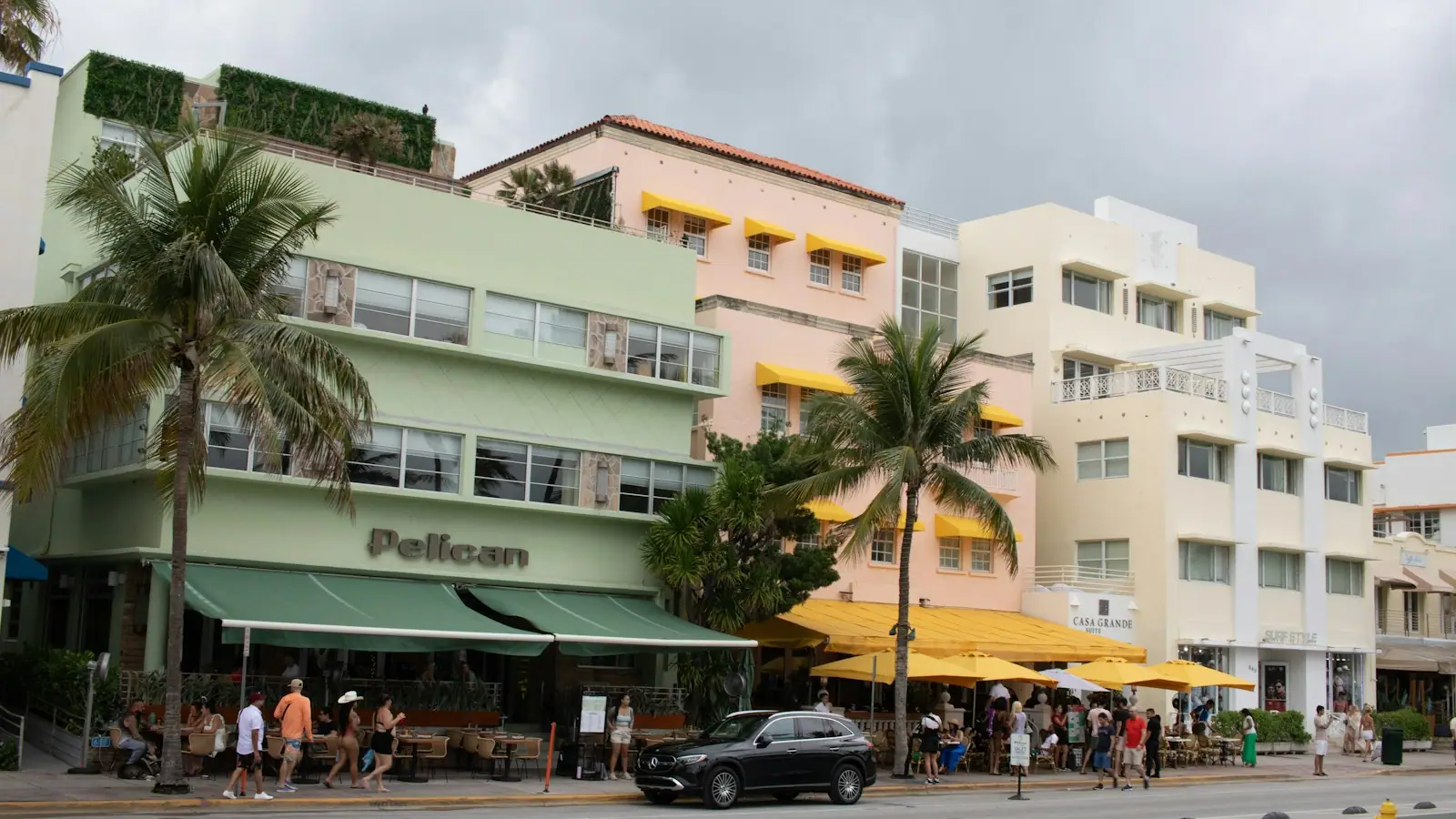 A group of people walking down a Miami Beach street lined with tall buildings